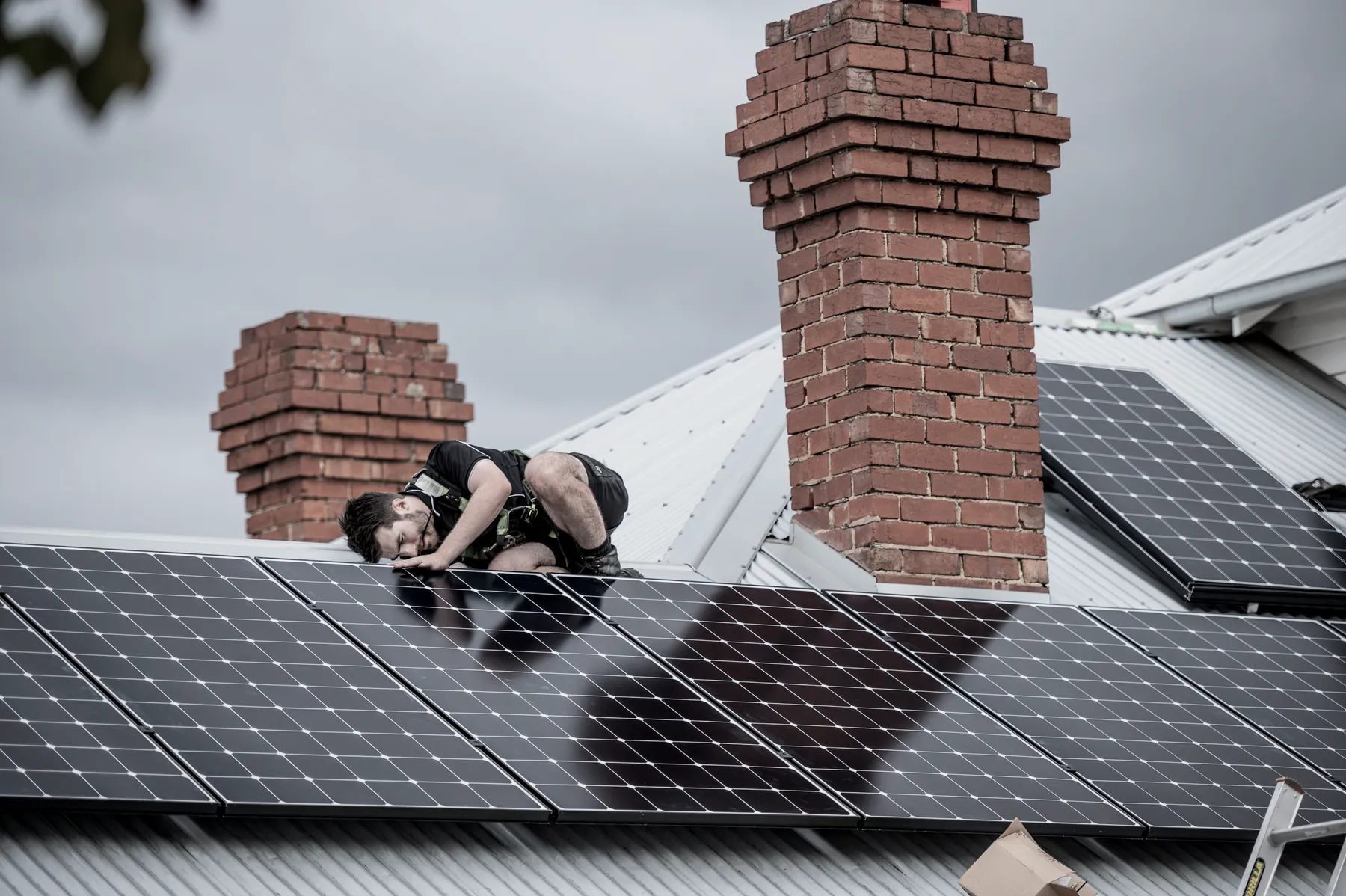 An installer fitting solar panels on a roof between two brick chimneys